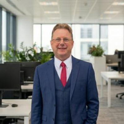 David_Koback_400x400 Adult man in a dark blue suit standing in an open-plan office