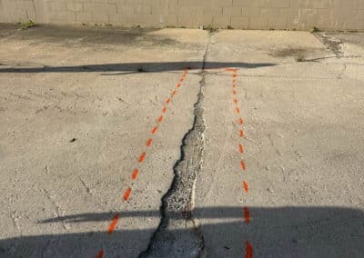 Morelli – Clinton Township, Michigan 6 Cracked light gray concrete surface with orange dashed lines outlining a rectangular area