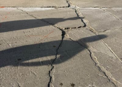 Morelli – Clinton Township, Michigan 2 Cracked concrete parking area with a beige block wall and bollard