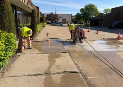 Morelli – Clinton Township, Michigan 8 Workers cutting and spraying water on a concrete sidewalk in a parking lot area
