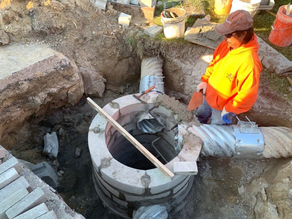 Concrete Pipe Installation Site Worker at a construction site with a trench and large circular concrete pipe